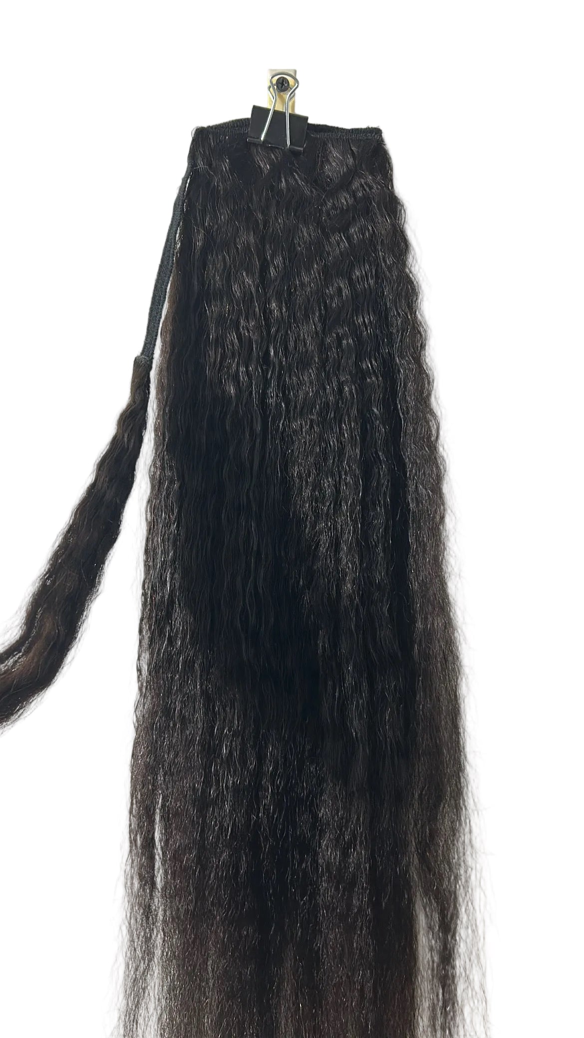 Long, dark brown to black Kinky Straight hair extension wrap-around Ponytail clipped to a white wall, with a small section of hair held on the left side.